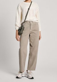 Beige hoch taillierte Hose, kombiniert mit einem cremefarbenen Strickpullover mit strukturiertem Muster, ergänzt durch eine kleine olivgrüne Umhängetasche und Turnschuhe.