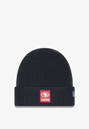 Beanie en maille bleu marine avec un revers, arborant un patch carré rouge sur lequel est inscrit "SF" et "San Francisco 49ers" en lettres blanches.