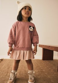 Svetloružová mikina s balónovými rukávmi a spinkou pandy, vrstvená cez plisovanú sukňu s vzorom houndstooth, kombinovaná s béžovými teniskami a krémovými ponožkami.