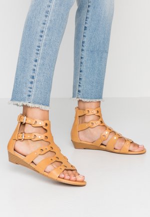 Brune læder kilehælssandaler med flere stropper med runde udskæringer og justerbare spænder. Struktureret kilehæl giver stabilitet.