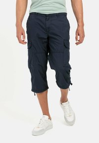 Marine cargo shorts met meerdere zijzakken, een trekkoord aan de onderkant en een lichte, gestructureerde stof, gecombineerd met witte sneakers.