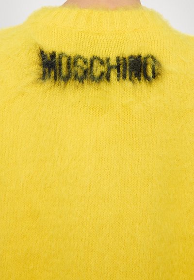 Maglione giallo lavorato a maglia con una texture morbida. Logo nero "MOSCHINO" ben visibile sul colletto posteriore. Collo tondo classico.