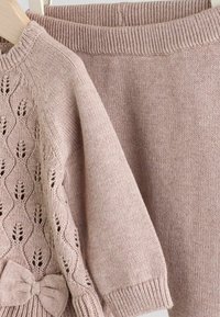 Haut en tricot rose avec un motif en dentelle et un détail de nœud, accompagné d'une jupe rose unie ; les deux comportent des poignets et des ceintures côtelés.