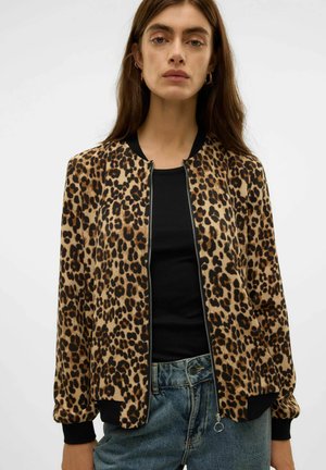 Jas met luipaardprint en een beige basis, zwarte geribbelde cuffs en kraag. Ritssluiting aan de voorkant en een relaxte pasvorm. Gedragen over een zwart top.