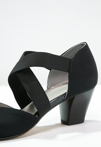 Sandal con tacco nero e design a strappo incrociato realizzato in tessuto morbido. Presenta una punta arrotondata e un tacco a blocco di altezza media. Texture della superficie liscia.