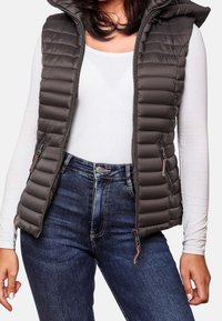 Vadderad väst i mörkgrått med huva, med horisontell quiltning, två sidofickor med dragkedja och dragkedjeöppning framtill. Matchas med blå jeans.