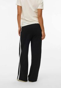 Czarne dresy z białymi paskami po bokach i luźnym krojem, wykonane z miękkiego materiału, z prostą nogawką i elastycznym pasem.