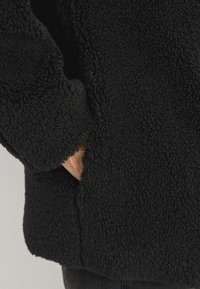 Mustang fleece-takki, jossa on teksturoitu pinta, rento istuvuus ja sivutaskut, näkyvät ompeleet helmassa ja hihojen reunoissa.