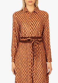 Abito camicia marrone con motivo, caratterizzato da una chiusura frontale con bottoni, maniche lunghe, vita cintrata e un design geometrico in tonalità di arancione e crema.