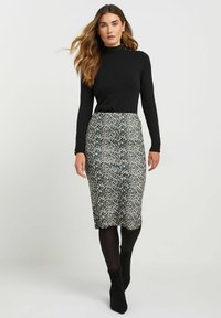 Schwarzes Langarmoberteil kombiniert mit einem knielangen Rock im grünen und cremefarbenen Leopardenmuster. Das Outfit wird durch schwarze Knöchelstiefel ergänzt.