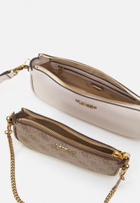 Kaksi laukku: sileä beige nahka kullanvärisellä varustuksella ja kuvioitu ruskea ketjuhihnalla. Molemmissa on kullanväriset vetoketjut ja logot yksityiskohtina.