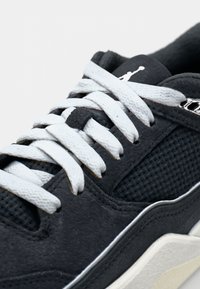 Mørkegrå ruskindsneakers med hvide snørebånd og mesh-detaljer. Har en tekstureret overflade og et markant logo-aksent på siden.