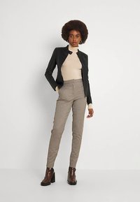 Geacă neagră din piele, cu croială strâmtă, helancă bej, pantaloni maro cu model houndstooth și cizme maro lucioase cu toc și glezna acoperită. Vedere completă a corpului.