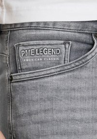 Sive traperice s vidljivom etiketom na kojoj piše "PME LEGEND AMERICAN CLASSIC." Ravnog kroja s blagim izbljeđenjem i teksturiranim završetkom.