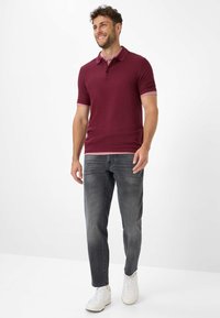 Polo a maniche corte bordeaux con colletto rosa a contrasto, abbinato a jeans grigi e sneakers bianche. Vestibilità casual, texture liscia.