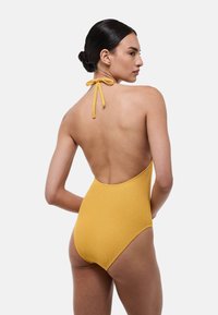 Maillot de bain une pièce jaune avec un tissu texturé, design à col halter et ouvertures de jambe haute, mettant en valeur un style de dos ouvert.