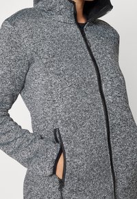 Szara kurtka zapinana na zamek, wykonana z tkaniny o fakturze; ma wysoki kołnierz, kieszenie na zamek oraz kontrastowe czarne wykończenia przy kapturze i mankietach.