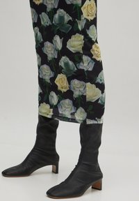 Bloemenjurk met zwarte achtergrond en rozenpatroon, gecombineerd met kniehoge zwarte leren laarzen met een spitse neus en blokhak.