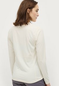 Lange mouw top in off-white stof, met een gladde textuur, voldoen ontwerp en naaddetails langs de rug voor extra structuur.