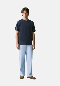 Laivastonsininen lyhythihainen t-paita yhdistettynä vaaleansinisiin raidallisiin leveälahkeisiin housuihin ja ruskeisiin slip-on -kenkiin, esitettynä valkoista taustaa vasten.