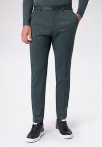 Ciemnozielone spodnie z fakturowanej tkaniny, o wąskim kroju, gładkim przodzie i paskach, połączone z czarnymi sneakersami na białych podeszwach.