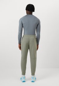 Fitted gray long-sleeve shirt, olive-green joggers with elastic waistband, and light blue athletic shoes. Minimalist design, smooth texture.