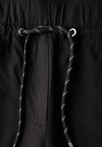 Zwarte shorts met een trekkoord met zilveren accenten, textuurstof en zakken. Het trekkoord heeft een contrasterend patroon.