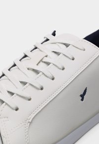 Λευκό δερμάτινο αθλητικό παπούτσι με λευκά κορδόνια, ραφές και ένα μικρό μαύρο λογότυπο πουλιού στο πλάι.