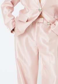 Light pink satin suit featuring a fitted blazer with a single button closure, and matching high-waisted trousers, smooth fabric texture.