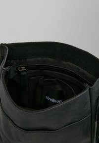 Interno di stivaletto in pelle nera con tasca con zip, fodera in tessuto morbido e una fascia interna intrecciata. Presenta un bordo cucito e un'etichetta del marchio.