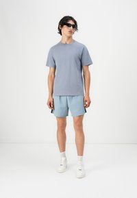 Lyseblå kortærmet t-shirt og matchende shorts. T-shirten er ensfarvet; shortsene har en struktureret stof. Båret med hvide sneakers.