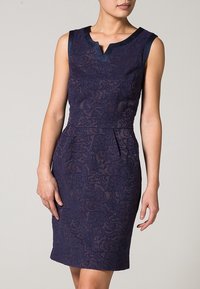 Námořnické krajkové šaty s přiléhavým siluetou, bez rukávů a výstřihem do V. Obsahují složité květinové vzory a hladký pas.