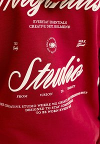 Tissu rouge avec texte blanc comportant des mots tels que « Studio », « Essentiels quotidiens » et des phrases sur la créativité et le confort.
