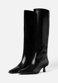 Bottes noires jusqu'aux genoux en cuir lisse, avec un bout pointu et un petit talon bloc, au design épuré et minimal.