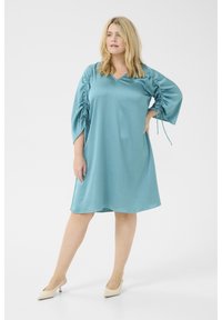 Robe en satin bleu-vert avec un décolleté en V, des manches froncées et des liens sur les côtés. Longueur au-dessus du genou, texture lisse et coupe décontractée.