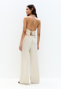 Dvojdielny outfit s topom bez chrbta so zaväzovaním a širokými pruhovanými nohavicami v krémovej farbe s jemnými modrými pruhmi.