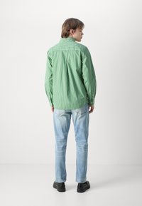 Πράσινο ριγέ πουκάμισο με μακριά μανίκια, συνδυασμένο με ανοιχτό μπλε τζιν και μαύρα παπούτσια. Το πουκάμισο διαθέτει χαλαρή γραμμή και γιακά.