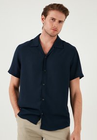 Korte mouwen overhemd van donker marineblauw stof, met een camp collar, knoopsluiting aan de voorkant en een gladde textuur. Gemaakt met een relaxte pasvorm en opgerolde mouwen.