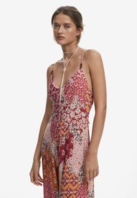 Vestido con un diseño de patchwork en tonos rojos, rosas y naranjas, que presenta patrones florales y geométricos, con tirantes finos y un ajuste relajado.