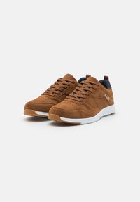 Brown suede sneakers with white rubber soles, textured design, and perforated accents. Laces and a small heel loop for easy wear.