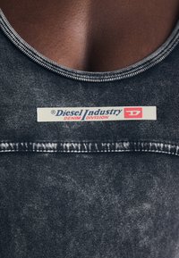 Tmavě modrý denimový top bez rukávů s kulatým výstřihem, který má bílou ševní linku a výraznou světlou nášivku "Diesel Industry DENIM DIVISION".