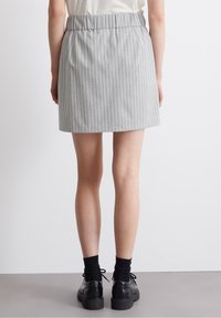 Falda a rayas grises con una cinturilla elástica, hasta la rodilla, que presenta rayas verticales. Combinada con zapatos negros y calcetas.
