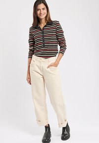 Gestreiftes Langarmoberteil in Schwarz, Rot und Creme, kombiniert mit Cremefarbener Jeans. Die Jeans haben umgeschlagene Säume und einen lockeren Schnitt. Schwarze Knöchelstiefel.