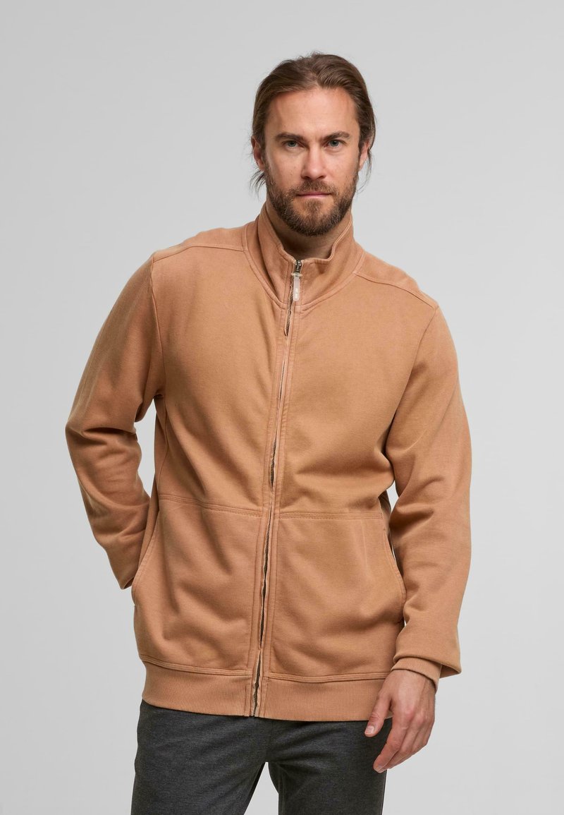 Beige Zip-Jacke aus weichem Stoff, mit hohem Kragen, gerippten Bündchen und zwei Fronttaschen mit versetzten Nähten sowie geradem Schnitt.