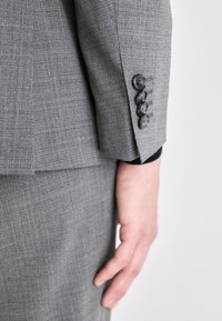 Blazer grigio caratterizzato da un tessuto testurizzato con un delicato motivo a quadri, quattro bottoni neri sui polsini e una vestibilità elegante e su misura.