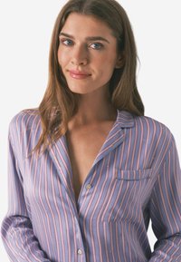 Chemise boutonnière violet clair avec des rayures verticales roses, une poche poitrine et un col. Fabriquée en tissu doux, elle a des manches longues.