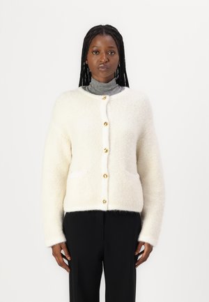 Cardigan blanc et duveteux avec un col rond, fermeture à boutons sur le devant et deux poches ; présente des boutons dorés et une texture douce.