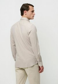 Camisa beige claro abotonada con una textura sutil, que presenta un cuello clásico y mangas largas, combinada con pantalones beige.