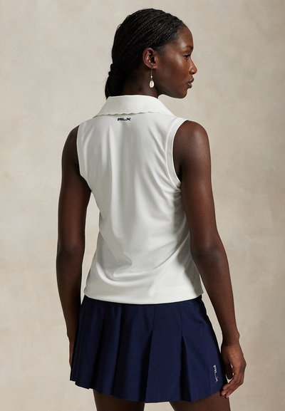 Αμάνικη λευκή πόλο με γιακά και κυματιστό τελείωμα. Συνδυάζεται με μπλε σκουρόχρωμη πλισέ φούστα. Λογότυπο RLX στο πίσω μέρος.