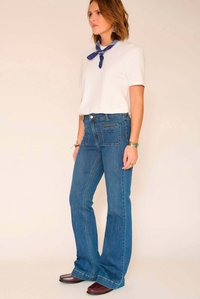 Jean en denim bleu évasé avec un design classique à cinq poches, porté avec un t-shirt blanc uni et un bandana bleu à motif.